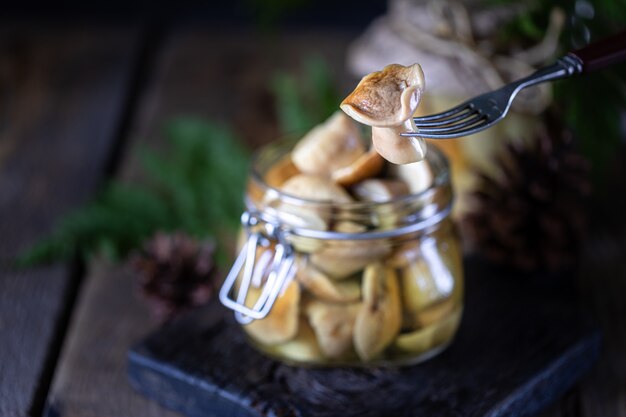 Setas en un frasco de vidrio. Hongos porcini fermentados caseros en una superficie oscura de madera Un hongo en un tenedor. Copia espacio