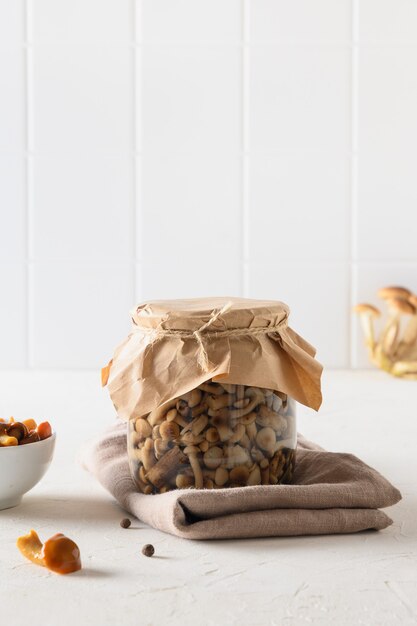 Setas de miel en escabeche en un recipiente y un tarro sobre un fondo blanco.