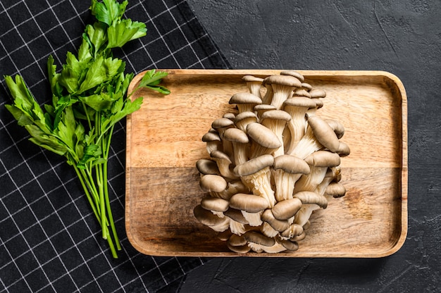 Setas de ostra crudas en un tazón de madera con perejil. Alimentos orgánicos. Vista superior.