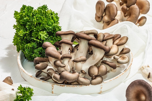 Setas de ostra frescas en un plato de cerámica con perejil Ingrediente saludable para cocinar comida vegana Fondo blanco luz dura sombra oscura plano yacía de cerca