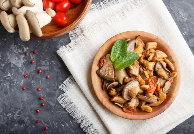 Setas de ostra fritas con tomates en placa de madera sobre negro