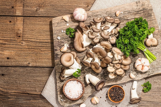 Setas de ostra listas para cocinar Especias de perejil fresco y ajo Sombras oscuras de luz dura de moda vista superior de fondo de madera vieja