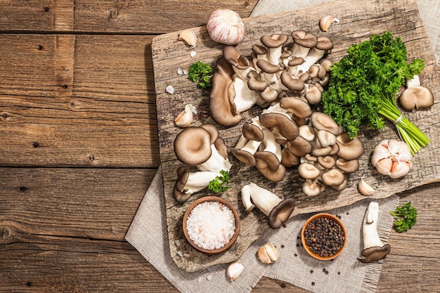 Setas de ostra listas para cocinar Especias de perejil fresco y ajo Sombras oscuras de luz dura de moda vista superior de fondo de madera vieja