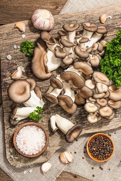 Setas de ostra listas para cocinar Especias de perejil fresco y ajo Sombras oscuras de luz dura de moda vista superior de fondo de madera vieja