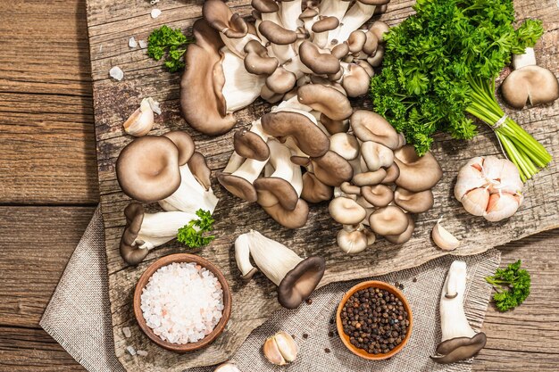 Setas de ostra listas para cocinar Especias de perejil fresco y ajo Sombras oscuras de luz dura de moda vista superior de fondo de madera vieja