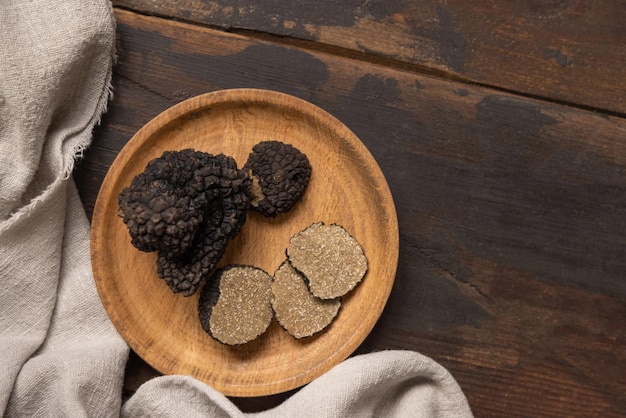 Setas de trufas negras enteras y en rodajas en un plato de madera sobre una mesa de color marrón oscuro espacio de copia plana