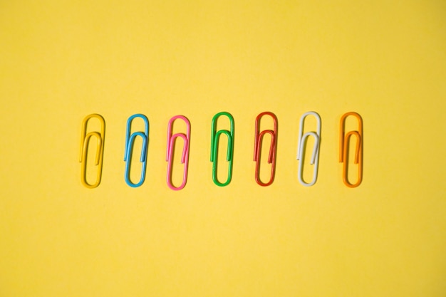 Sete clipes de papel de cores diferentes isolados em um fundo amarelo para usar o elemento de design