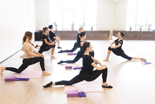 Sete dançarinas se aquecendo com exercícios de alongamento para flexibilidade durante a aula no pavilhão esportivo branco Ativo estilo de vida saudável hobby recreação bem-estar conceitos de perda de peso