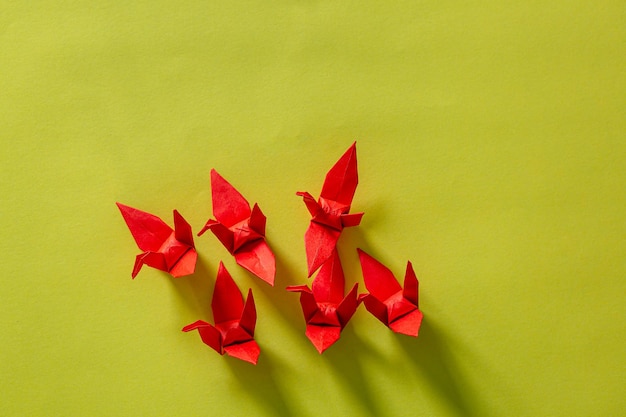 Sete pássaros de origami vermelhos estão voando liderando por um pássaro rosa isolado em brancoGrua de papel de origami vermelho