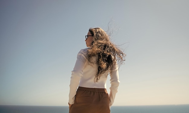 Seu cabelo está fluindo ao vento Mulher com cabelo comprido fica no mar Menina elegante com penteado ondulado