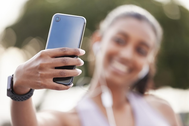 Seu telefone está cheio de fotos de seu progresso. Closeup tiro de uma jovem desportiva usando fones de ouvido e tirando selfies durante o exercício ao ar livre.