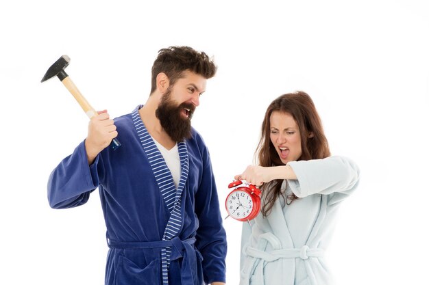 Seu tempo adiantado. Casal com sono apaixonado no tempo da manhã. Hipster zangado e mulher quebrando o despertador com martelo, tempo perdido. O tempo mostrará.