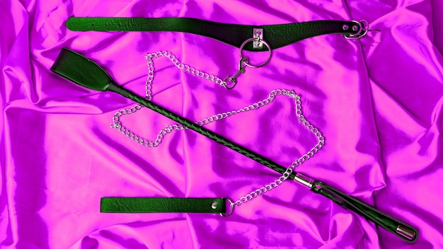 Sexspiele für Erwachsene BDSM-Artikel Lederriemenhalsband mit Metallkettenleine und Peitsche auf einem roten Satinblatt