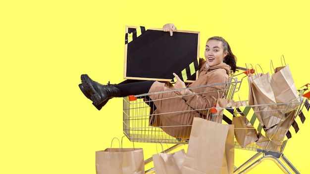 Sexta-feira negra, uma menina está sentada em uma cesta de compras e aponta alegremente para o quadro em suas mãos