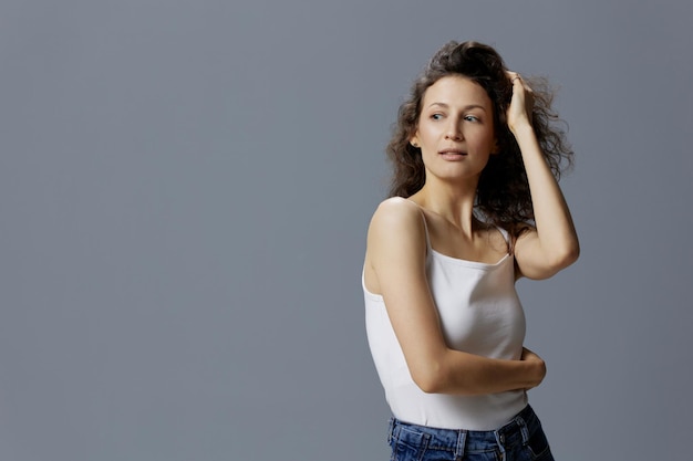 Foto sexy adorável mulher bonita em camisa branca básica toca o cabelo abraça-se olha para o lado posando isolado sobre fundo azul cinza pessoas estilo de vida emoções conceito espaço de cópia