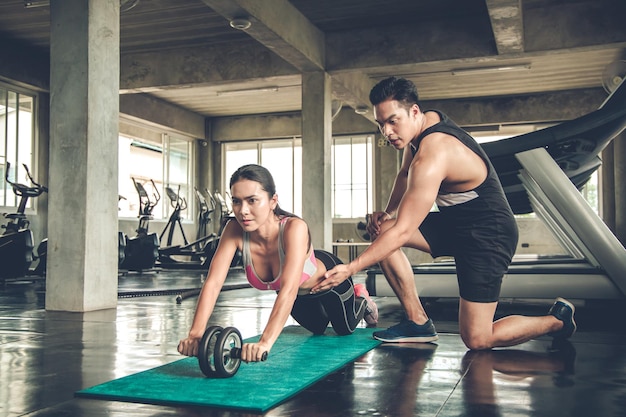 Sexy asiatische Frau Workout durch ab Rad auf Yoga-Matten-Übung mit Mann sind Trainer im Fitnessstudio. Konzept der Übung im Fitnessstudio.