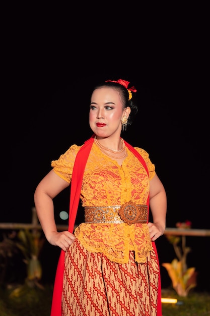 Sexy balinesische Frau mit Make-up, während sie ein orangefarbenes Kleid namens Kebaya trägt, das nach dem Tanzen tapfer posiert