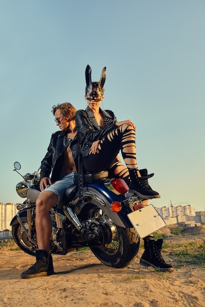 Sexy Bikerpaar auf dem Vintage Custom-Motorrad, Mädchen in einer Kaninchenmaske. Junge schöne Paar-Hipster in stilvoller Kleidung für Motorrad auf der Straße, Outdoor-Porträt