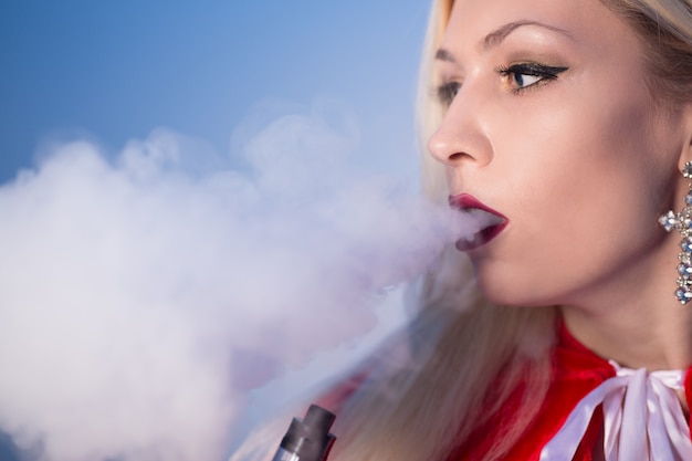 Sexy blonde Frau im Sankt-Kostüm, die elektronische Zigarette raucht