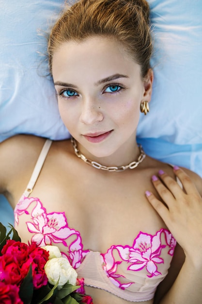 Foto sexy blonde frau mit blauen augen in unterwäsche mit einem blumenstrauß auf dem bett