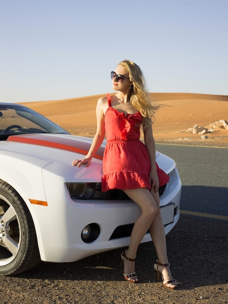 Sexy blondes Mädchen sitzt auf Cabrio-Motorhaube in der Wüste