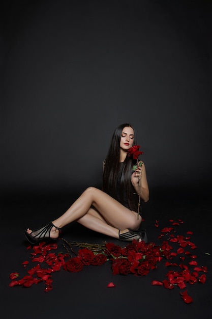 Sexy Brünette mit einem Strauß roter Rosen auf dem Boden, lange Haare, nackte Körperteile, sexy Porträt einer Frau Rosenblüten