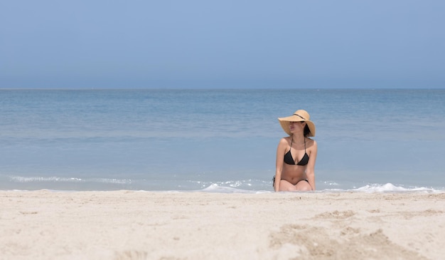 sexy brünettes Model im schwarzen Bikini und blauem Hut am Strand