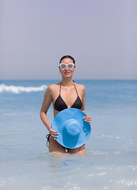 sexy brünettes Model im schwarzen Bikini und blauem Hut am Strand