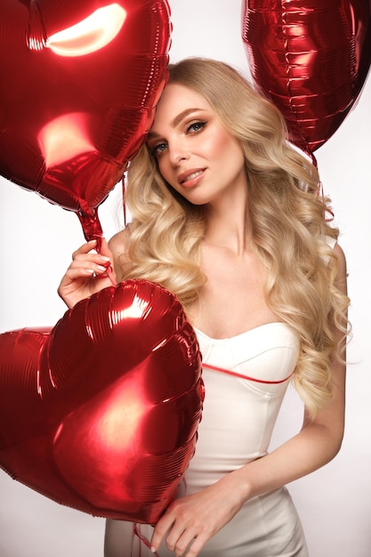 Sexy Frau in weißem Kleid und Luftballons mit Herzen posiert am Valentinstag im Studio