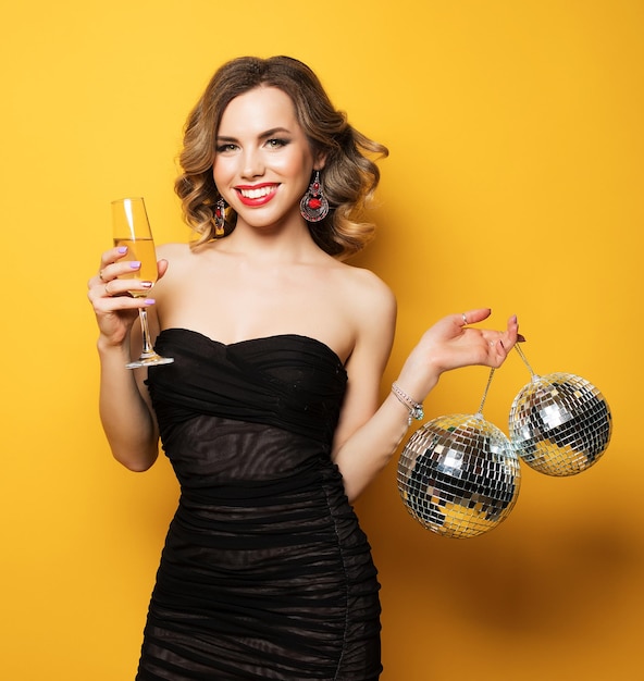 Sexy Frau mit einem Glas Weißwein und Discokugel auf gelbem Hintergrund