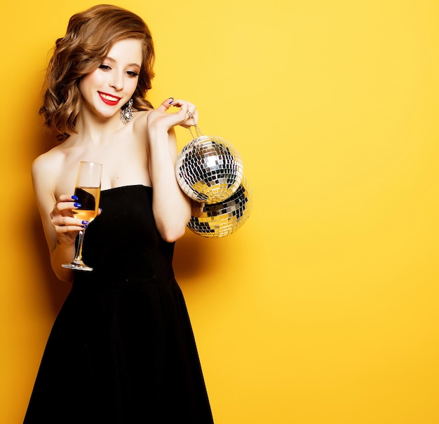 Sexy Frau mit einem Glas Weißwein und Discokugel auf gelbem Hintergrund