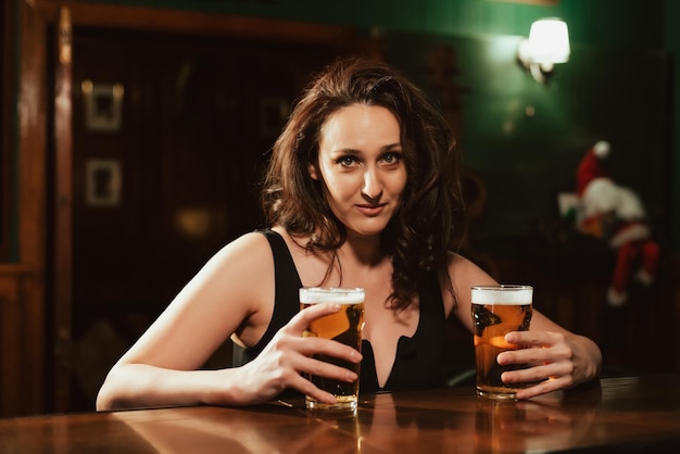 Sexy Frau mit großen Brüsten mit zwei Gläsern Lagerbier in der Hand an der Bar