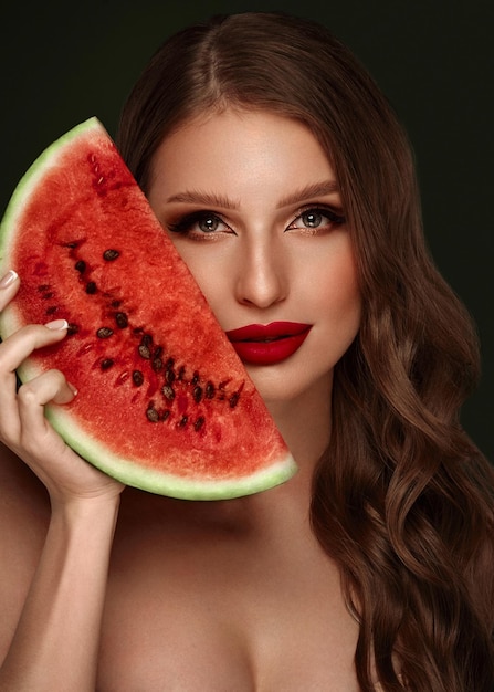 Sexy Frau mit klassischem Make-up der Locken und roten Lippen hält eine Wassermelone in ihren Händen Schönheitsgesicht