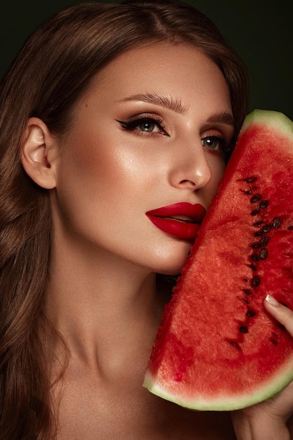 Sexy Frau mit klassischem Make-up der Locken und roten Lippen hält eine Wassermelone in ihren Händen Schönheitsgesicht