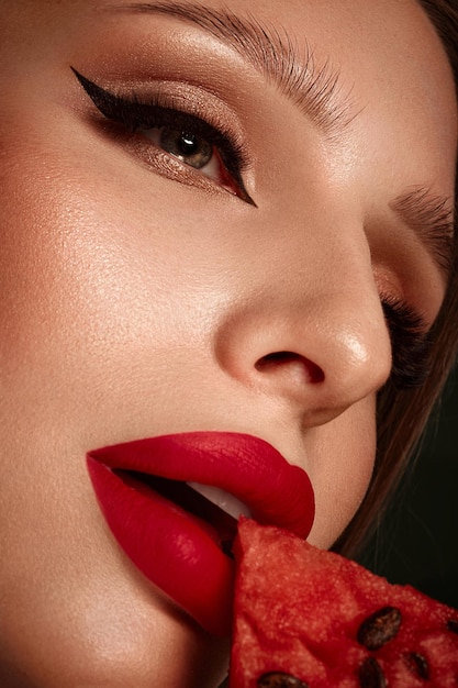 Sexy Frau mit klassischem Make-up der Locken und roten Lippen hält eine Wassermelone in ihren Händen Schönheitsgesicht