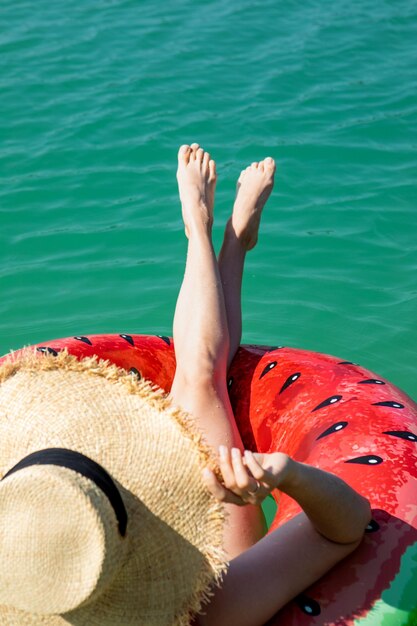 Sexy Frauenbeine auf aufblasbarem Ring, der im Kopienraum des blauen Seewassers schwimmt