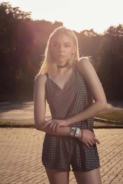Sexy gebräuntes blondes Model mit langen Haaren, das einen schwarzen Strampler trägt und in Sonnenblendung posiert