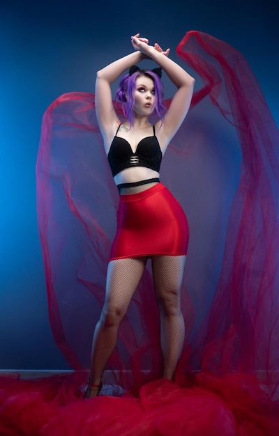 Sexy Girl in einem roten Rock und einem Bustier posiert erotisch mit einem transparenten Stoff