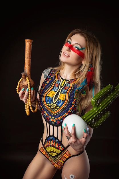 Sexy Hippie-Mädchen posiert mit Bong zum Rauchen von Marihuana in einem hellen Badeanzug auf dunklem Hintergrund