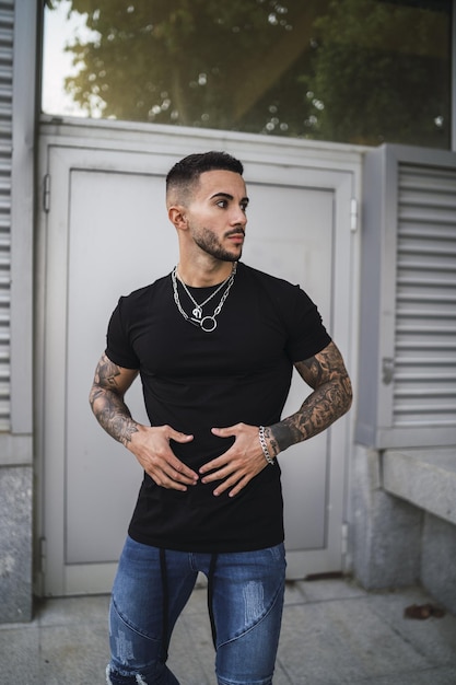 Sexy hombre tatuado con una camisa negra ajustada y jeans de pie en el fondo de una puerta