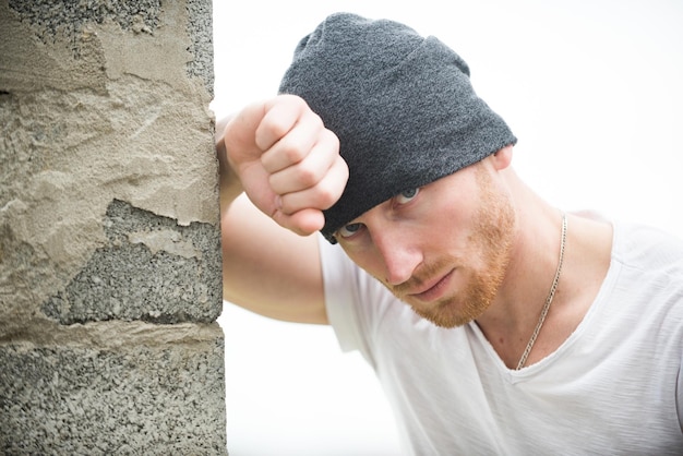 Foto sexy ingwer unrasierter brutaler mann mit beanie-mütze, der in der nähe der wand steht stil und mode des mannes brutaler männlicher mann nahaufnahme studioporträt schöner mann mit ingwerroten haaren