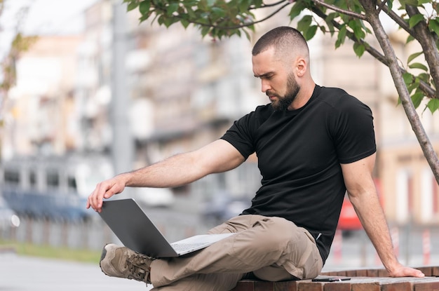 Sexy jovem forte com barba sentado trabalho na Internet ao ar livre