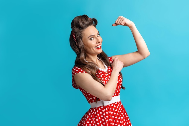 Sexy jovem pinup em vestido retrô mostrando seus músculos bíceps no fundo azul do estúdio