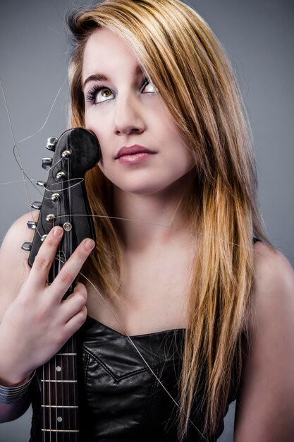 Sexy joven rubia vestida de cuero negro con guitarra eléctrica negra con mirada pensativa