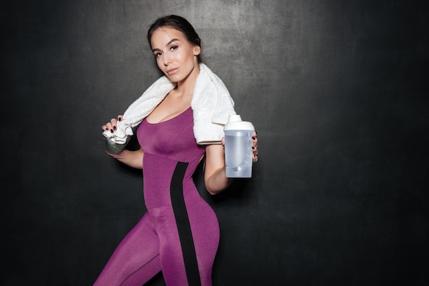 Sexy junge Frau in der Sportbekleidung stehend und Wasserflasche zeigend