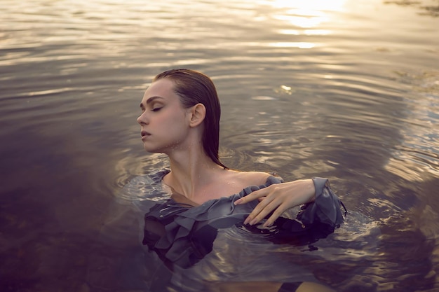 Foto sexy junge frau in einem grauen kleid liegt im wasser bei sonnenuntergang im fluss