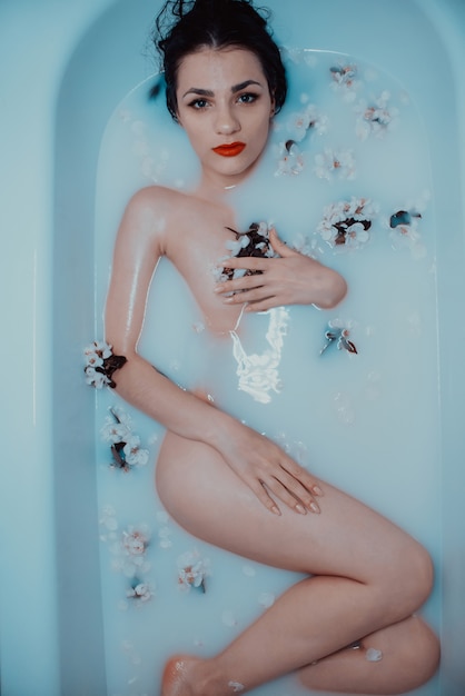 Sexy junges kaukasisches Mädchen im Bad mit Milch- und Apfelblüten