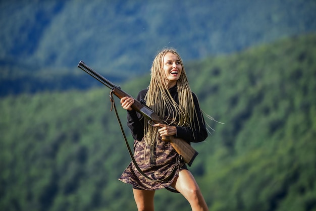 Sexy Kriegerin Sie ist Kriegerin Krieger Berge Landschaft Hintergrund Feministisches Mädchen Jagdsaison Frau attraktives langes Haar hübsches Gesicht halten Gewehr für die Jagd Gefährliches Mädchen Verteidigungskonzept