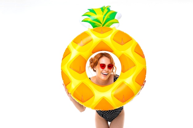 Sexy Mädchen in einem Badeanzug in einem Schwimmkreis in Form von Ananas im Urlaub auf einem weißen Hintergrund