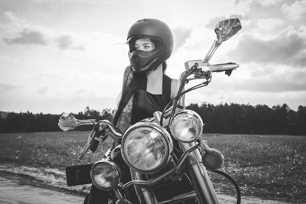 Sexy Mädchen in einem Lederanzug und Helm posiert auf einem Motorrad bei Sonnenuntergang. Reisekonzept. Gemischte Medien